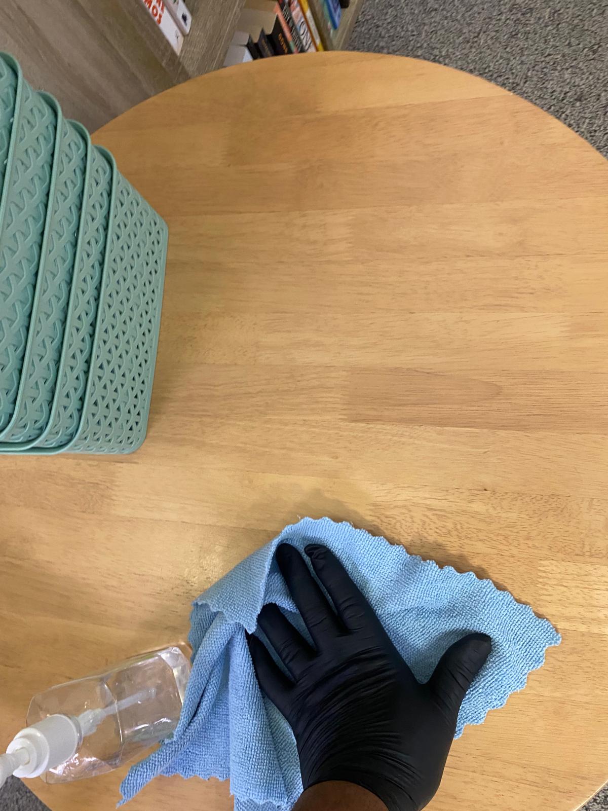 Cleaner wiping a wooden table with a microfibre cloth